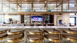 Zona de bar con televisión, taburetes y una barra llena de botellas.