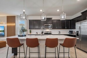 A modern kitchen with dark cabinets, stainless steel appliances, and a central island with bar stools. - Disney Dream Home Mario, Frozen & Minions (Davenport)