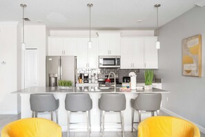 A modern kitchen with white cabinets, stainless steel appliances, and a central island with bar stools. - The Gatsby Retreat Luxe 4BR Townhome With Private Pool Oasis (Kissimmee)