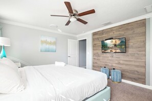 Ein Schlafzimmer mit Bett, Deckenventilator, Kunstwerken und einem Fernseher an der Wand.