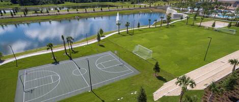 A basketball court with a water body and trees in the background.