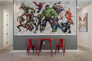 A hallway with a large superhero mural on the wall, a red table, and two red chairs. - Huge 9br/solara Resort/themed Rooms/games/disney! (Kissimmee)