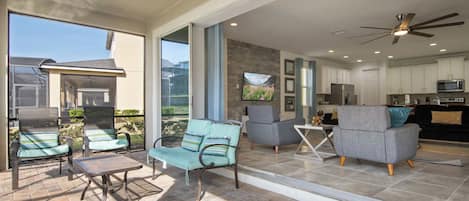 A spacious patio with outdoor seating, a ceiling fan, and a view of the surrounding landscape.