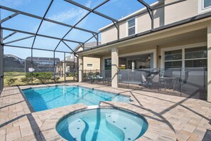 Ein Schwimmbecken mit Whirlpool, umgeben von einer überdachten Terrasse mit Gartenmöbeln.
