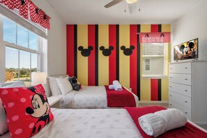 A hotel room with two beds, Mickey Mouse themed pillows, a red and yellow striped wall, a television, and a window with blinds. - Huge 9br/solara Resort/themed Rooms/games/disney! (Kissimmee)