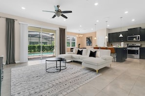 A modern living room with a sectional sofa, a coffee table, and a large window overlooking a pool. - Cozy 5BR Solterra Home w/ Private Pool (Davenport)