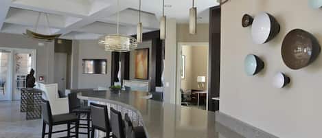 A modern kitchen with a curved island, bar stools, pendant lighting, and a wall-mounted light fixture.