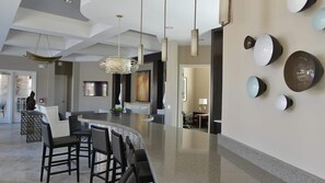 A modern kitchen with a curved island, bar stools, pendant lighting, and a wall-mounted light fixture. - Cozy 5BR Solterra Home w/ Private Pool (Davenport)