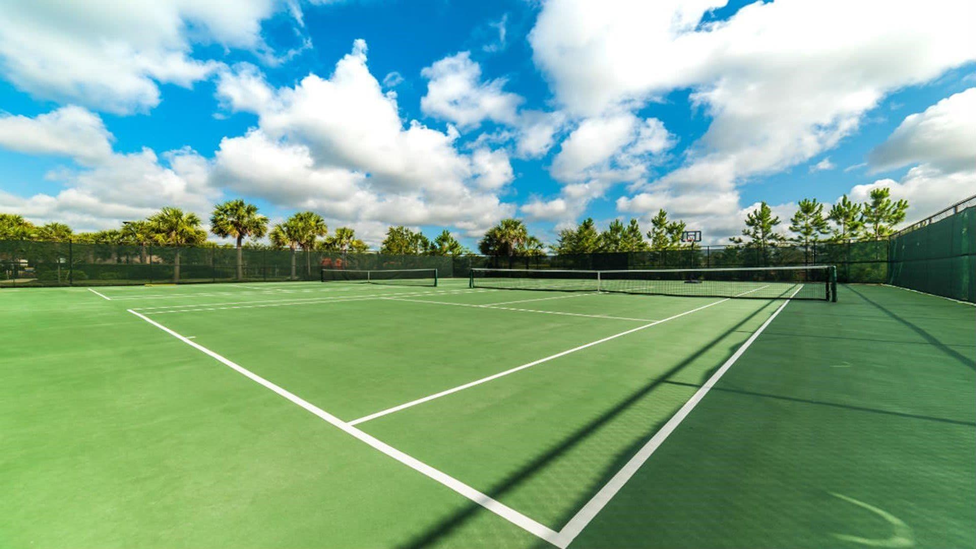 En tennisplan med nät, omgiven av träd och en klar himmel.