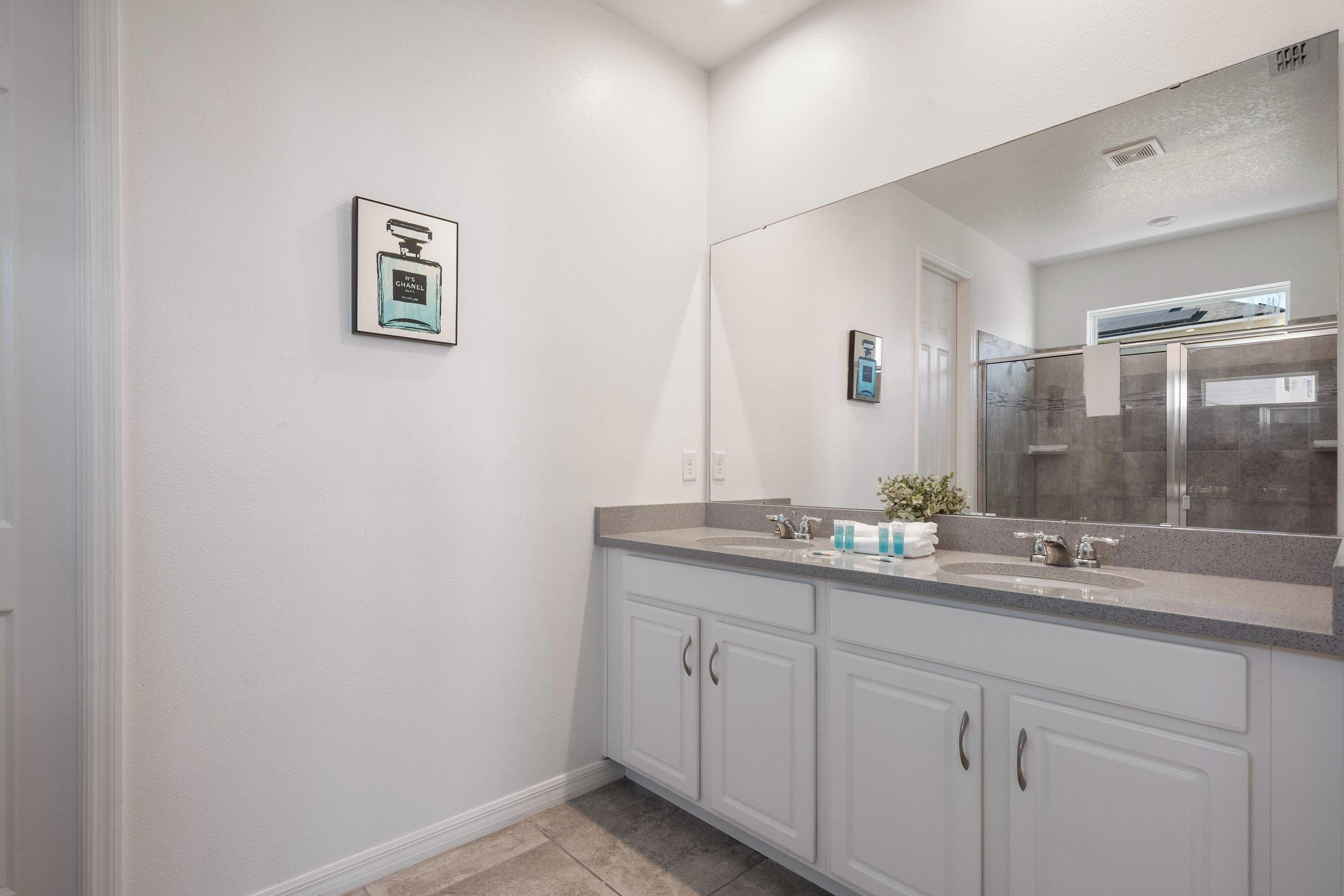 Une salle de bain moderne avec un grand miroir, des meubles blancs et un plan de toilette où sont posés les articles de toilette.