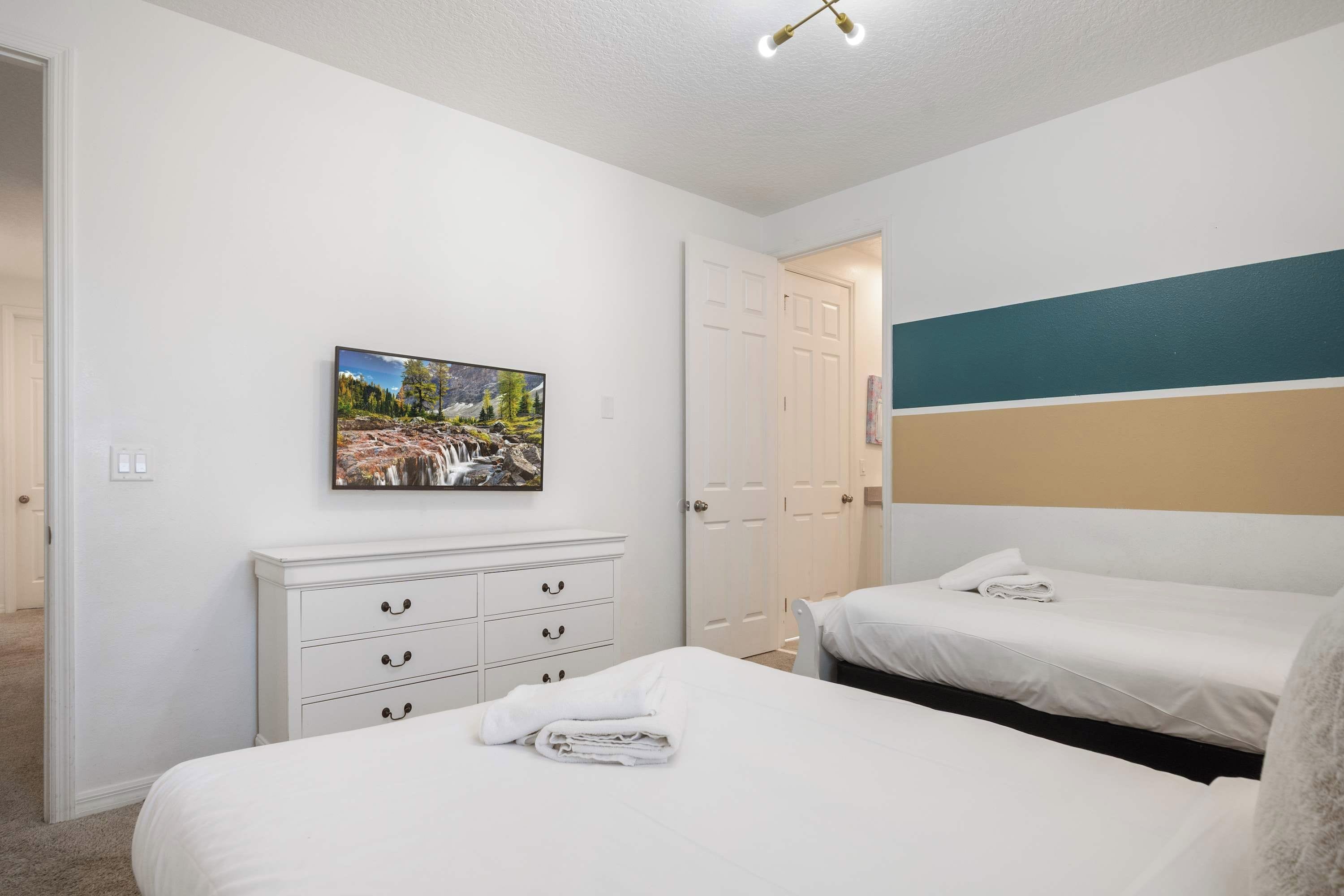 A bedroom with two beds, a white dresser, a painting, and a door.