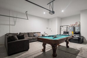 Ein Billardtisch in einem Raum mit einer Couch, einem Projektor und einem Durchlauferhitzer.