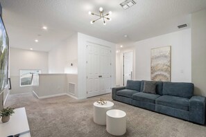 Un salon moderne avec un canapé gris, deux petites tables rondes et un luminaire suspendu au plafond.