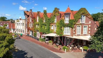A row of traditional brick buildings with red-tiled roofs, some with ivy, and a street with a cobblestone road.