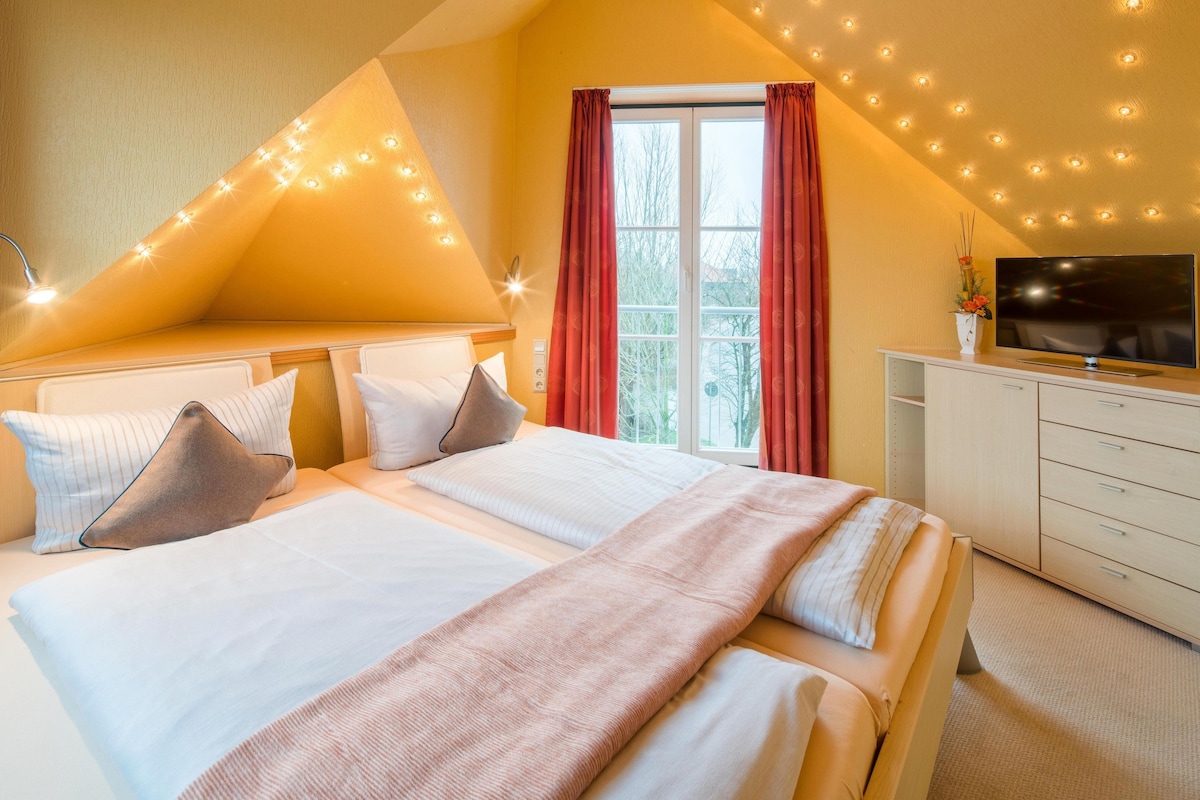 Un dormitorio con una cama grande, televisión y ventana con cortinas.