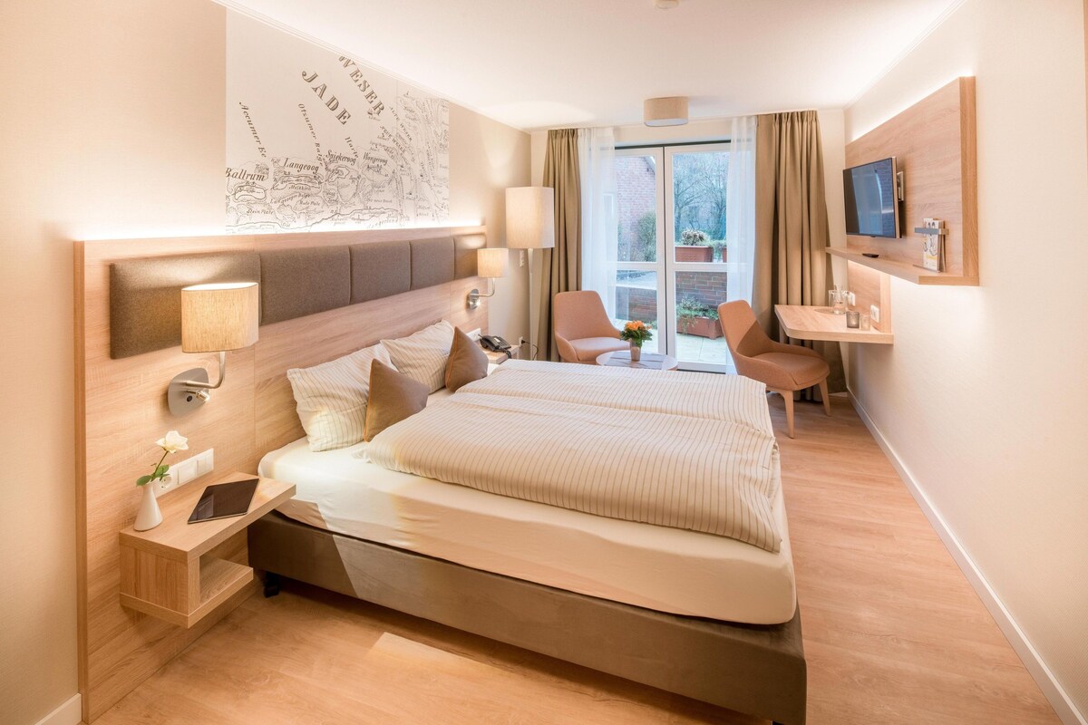 Una habitación de hotel moderna con una cama grande, mesitas de noche, un escritorio, una silla y un televisor.