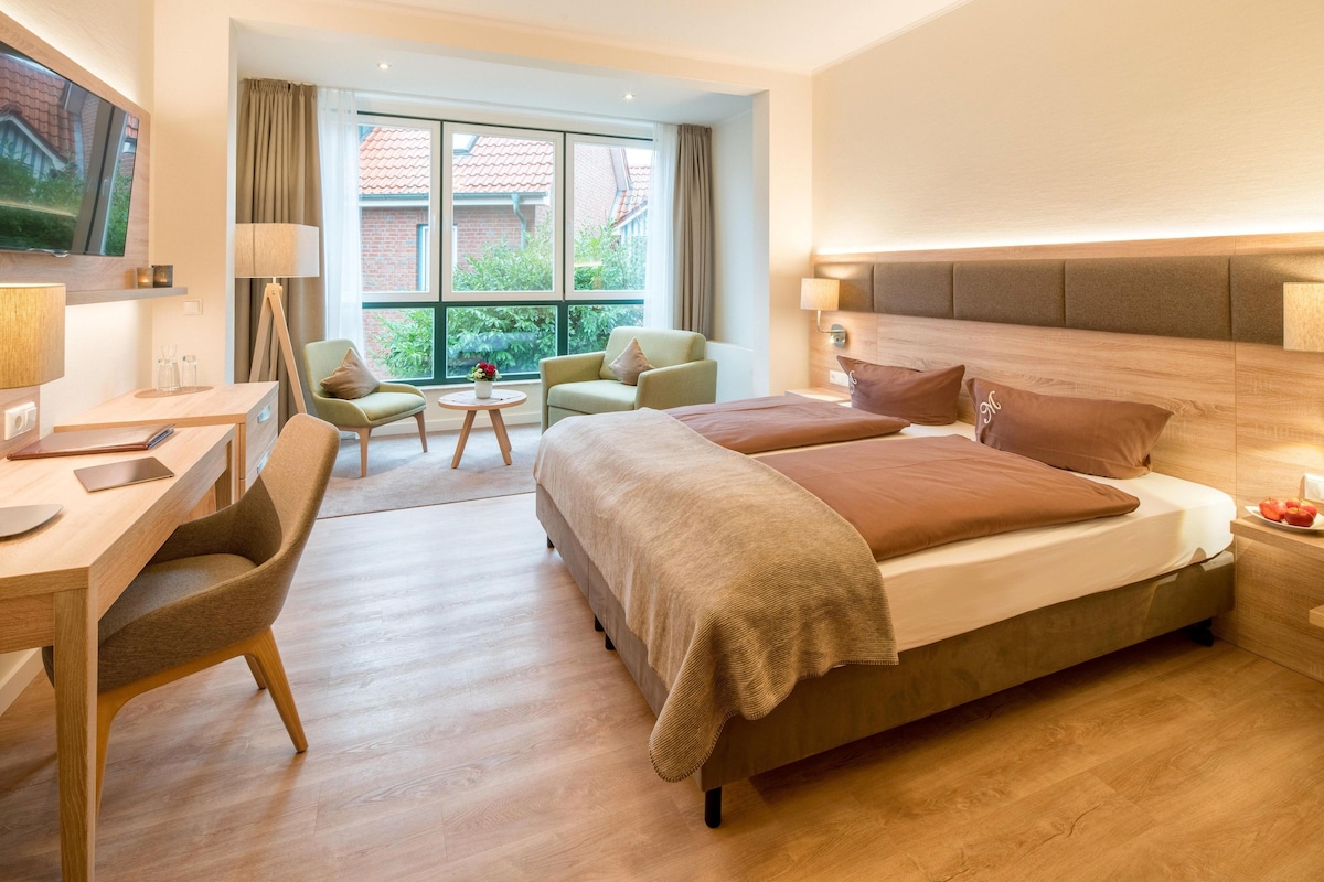 Habitación de hotel con cama, escritorio, silla, televisión y ventana con vista a un edificio de ladrillo.
