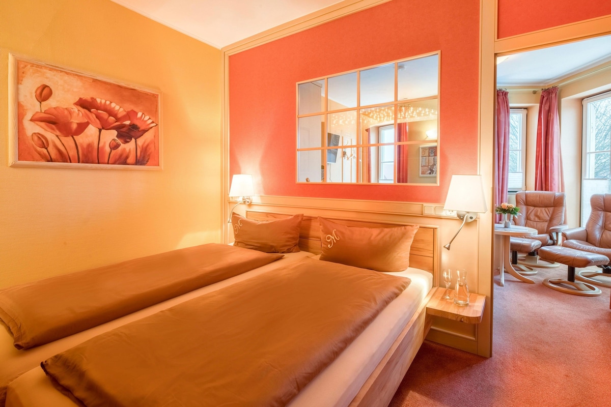 Habitación de hotel con dos camas, un cuadro, un espejo grande y un área de descanso con una mesa y sillas.