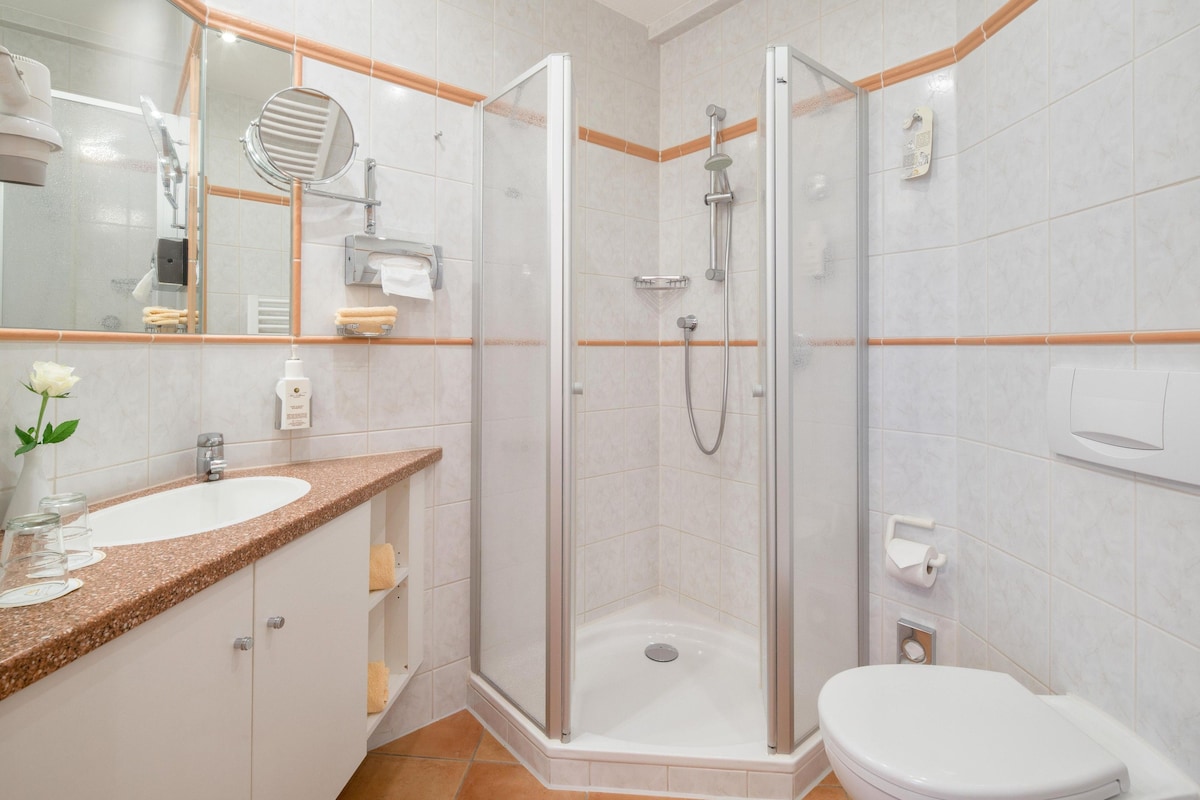 Un baño moderno con ducha envuelta en cristal, lavamanos con encimera de granito y un inodoro.