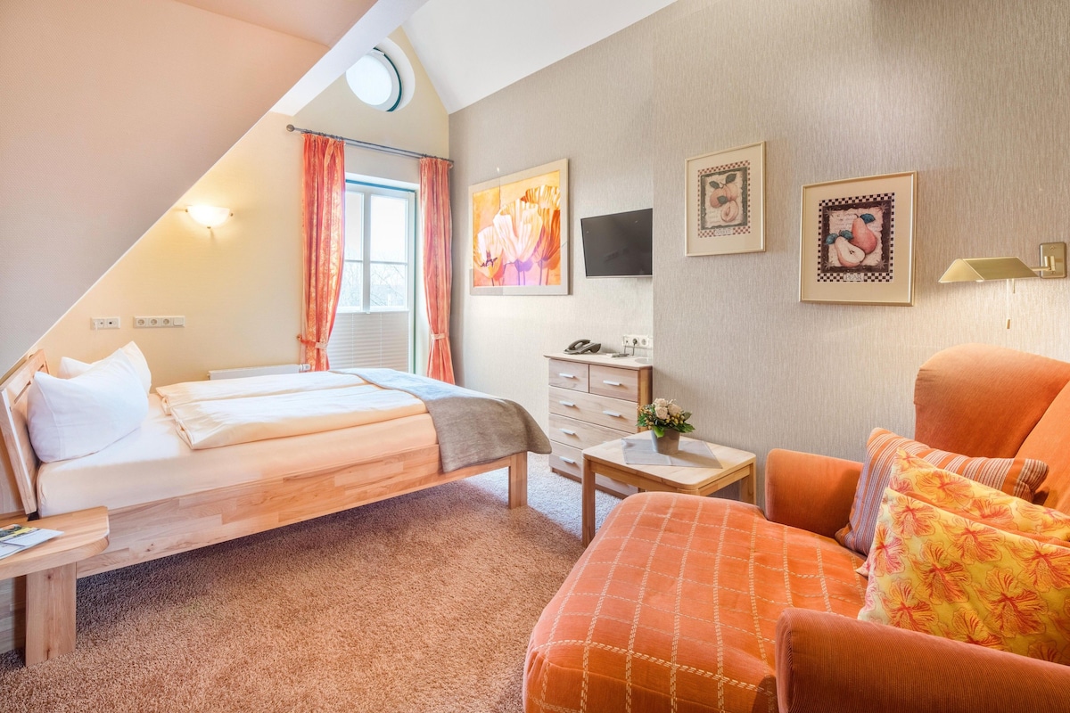 Une chambre d’hôtel équipée d’un lit, d’un bureau, d’une chaise, d’une télévision et décorée avec des œuvres d’art aux murs.