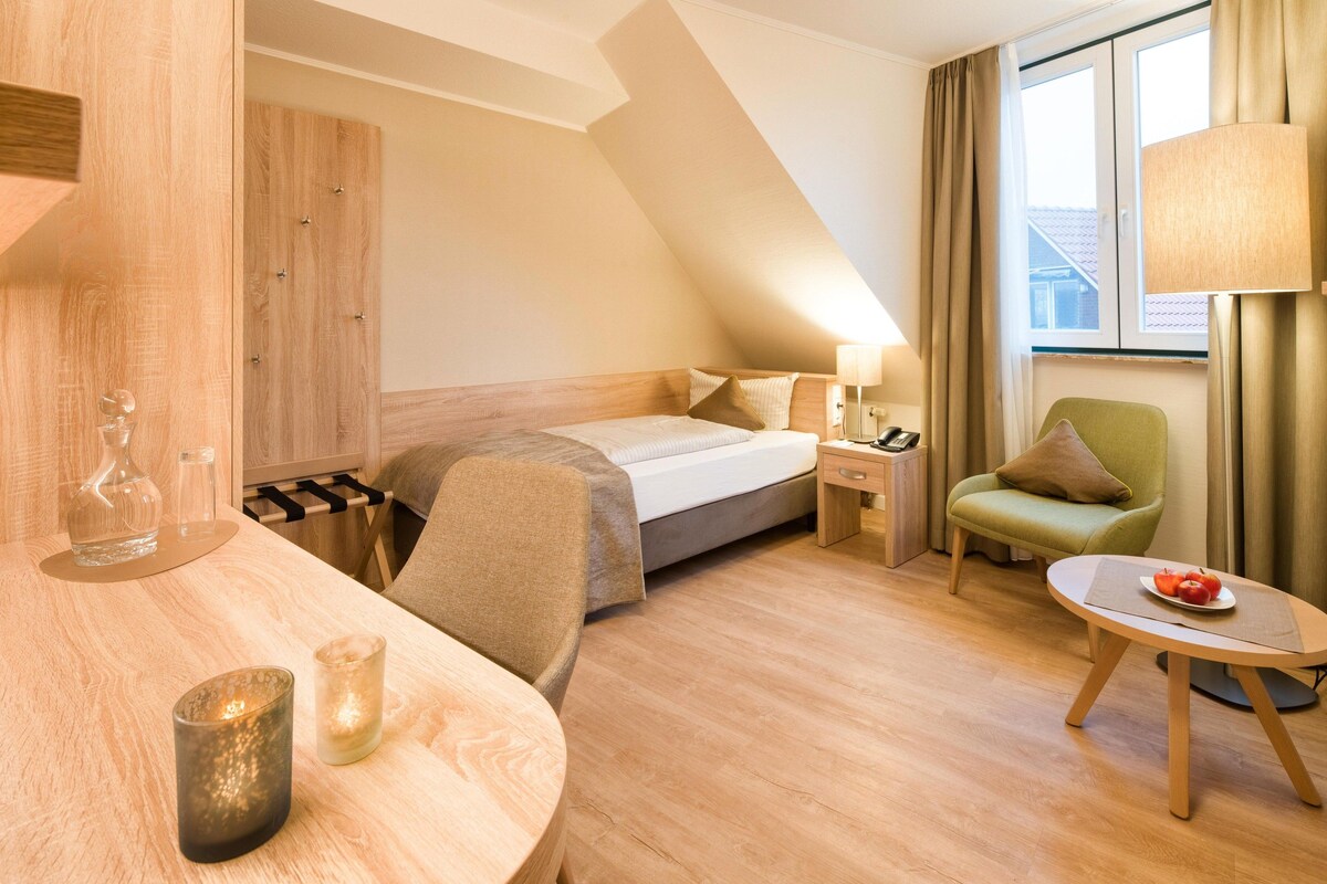 Una habitación de hotel con una cama, una silla, una mesa con manzanas y una lámpara.