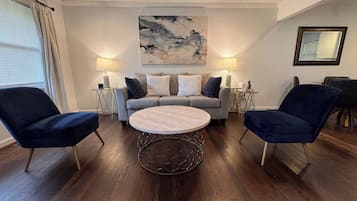 Ein modernes Wohnzimmer mit einem runden Couchtisch, zwei Sesseln, einem Sofa und einem Gemälde an der Wand.