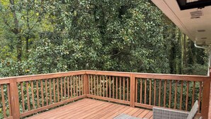 A wooden deck with a black table and wicker chairs, surrounded by dense foliage. - Updated 2BR | Private Deck | Near Decatur and EAV (Decatur)