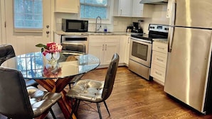 A modern kitchen with white cabinets, stainless steel appliances, a glass dining table, and a view of the outdoors through the windows. - Updated 2BR | Private Deck | Near Decatur and EAV (Decatur)