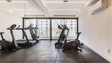 A gym with exercise equipment, large windows, and a view of buildings.