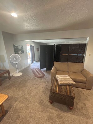 A living room with a beige sofa, a small ottoman, a standing fan, and a door leading to another room. - Relaxing 2 bdrm retreat near Zion with beautiful views sleeps eight, 2000 sq ft. (Hurricane)