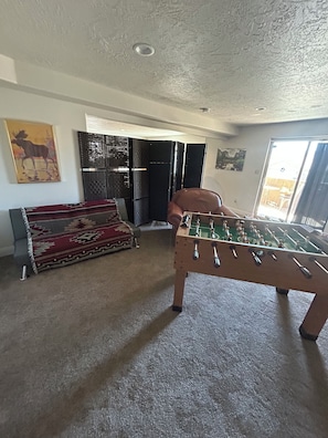 Ein Zimmer mit einem Fußballtisch, einer Couch und einem gemusterten Teppich.