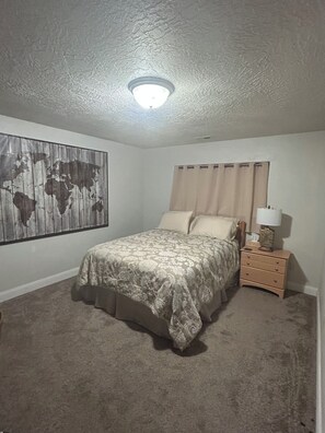 Un dormitorio con cama, una mesita de noche, una lámpara, un mapa del mundo en la pared y una luz en el techo.