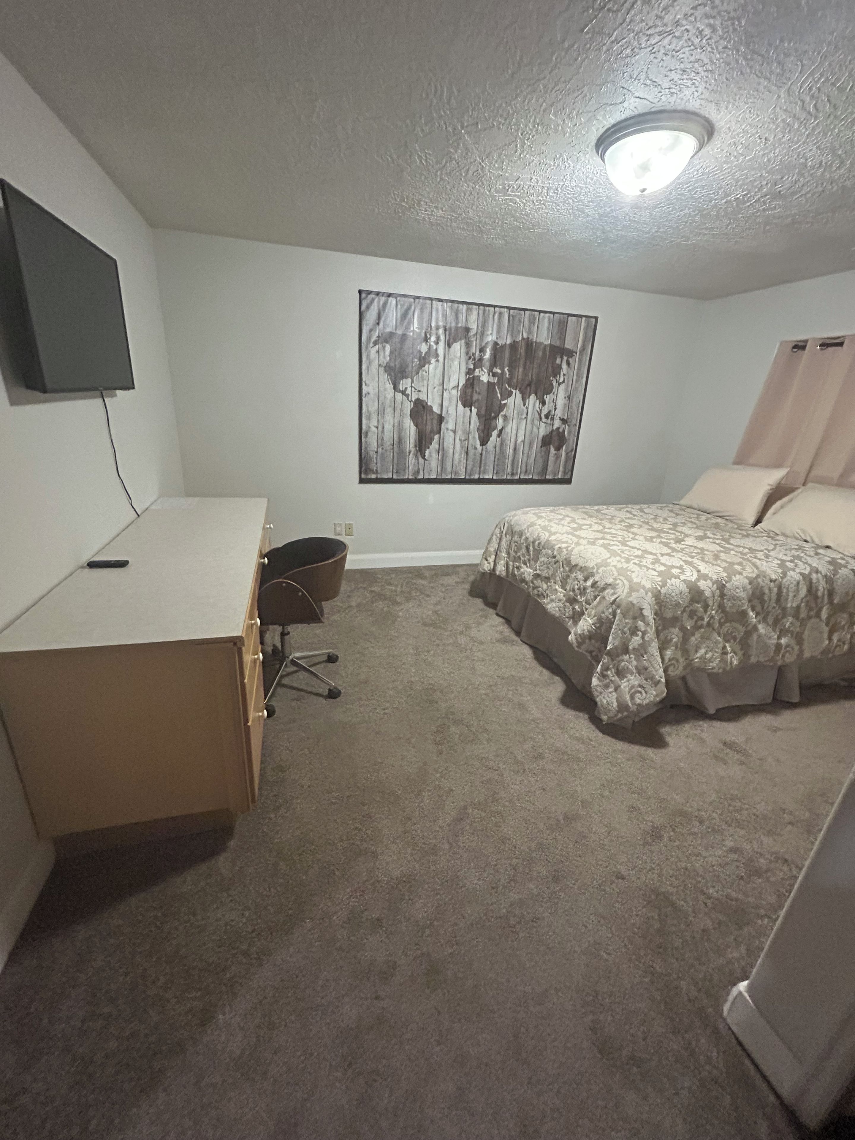 A bedroom with a bed, a desk, a chair, a world map on the wall, and a television on the wall.