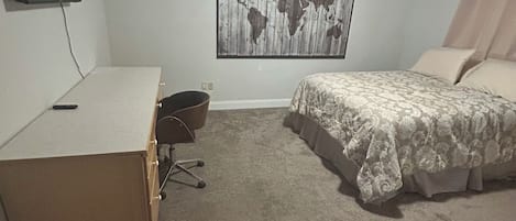 A bedroom with a bed, a desk, a chair, a world map on the wall, and a television on the wall.