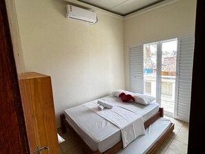 Ein Schlafzimmer mit einem Bett, einem Holzschrank und einem Fenster mit Blick auf Gebäude.