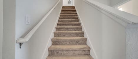 A staircase with carpeted steps and white walls, leading to a landing with a sign that reads 'love be kind.'