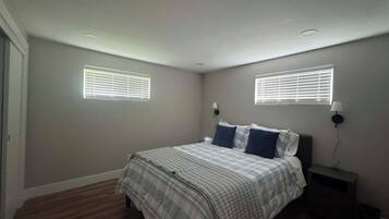 Un dormitorio con una cama, dos lámparas de noche y dos ventanas con persianas.