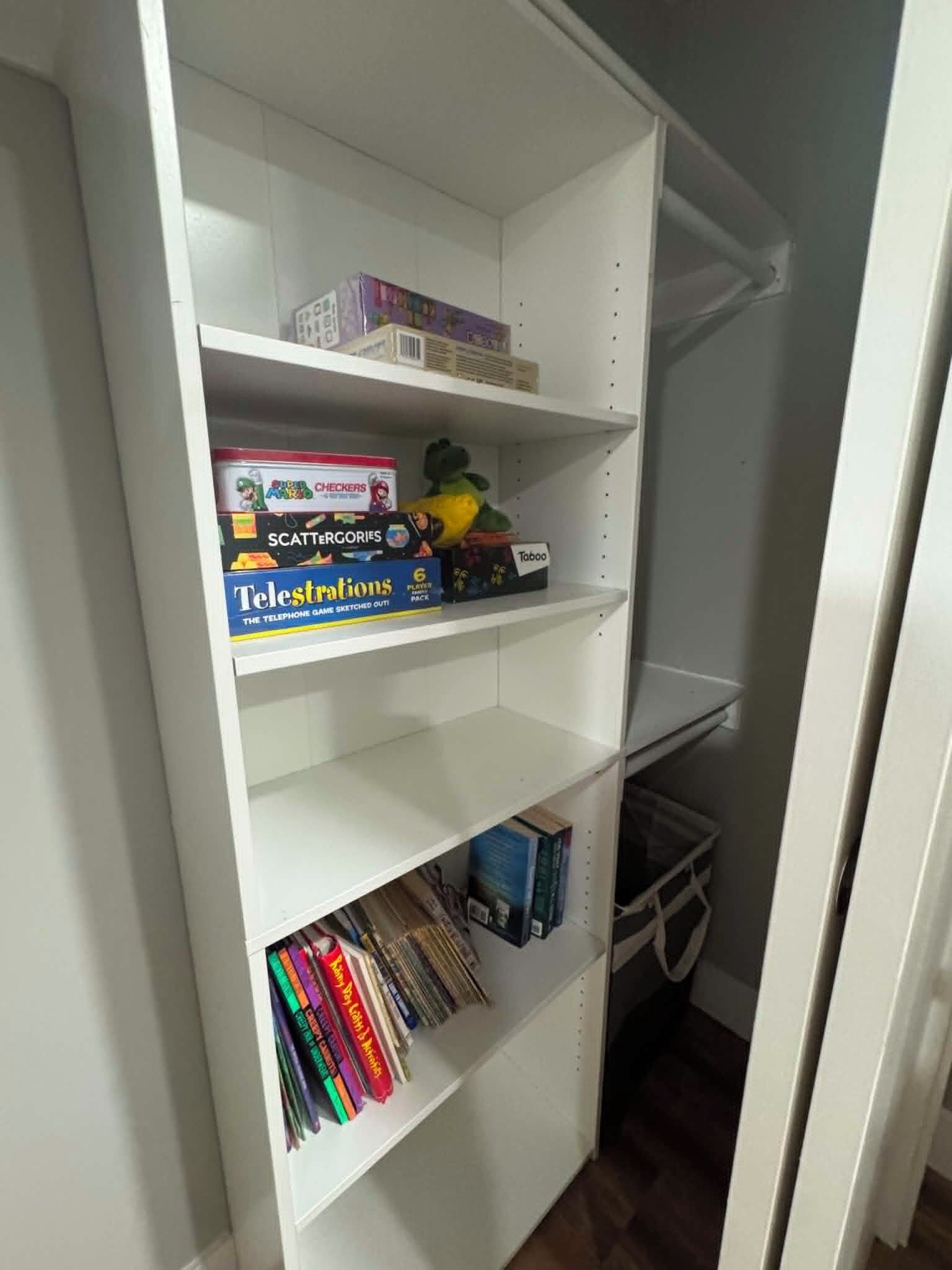 Un estante blanco con varios objetos, incluyendo un juego de mesa, un peluche y libros.