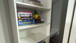 A white shelving unit with various items including a board game, a stuffed toy, and books. - Welcome to Rosehill (Dayton)