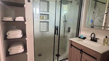 Ein modernes Badezimmer mit einer Duschkabine aus Glas, einem Holzbadezimmermöbel und einem eingebauten Regal mit gefalteten Handtüchern.