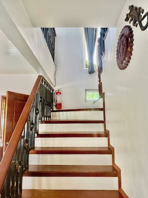 Una escalera de madera con barandillas metálicas, un extintor y decoración en la pared.