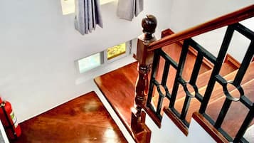 Eine Holztreppe mit schwarzer Geländer, ein Feuerlöscher auf der linken Seite und ein Fenster mit Vorhängen.