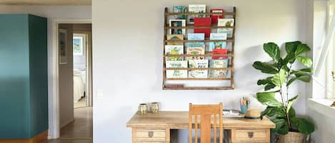 Una habitación con un escritorio de madera, una silla, una estantería con libros, una planta grande y una lámpara.