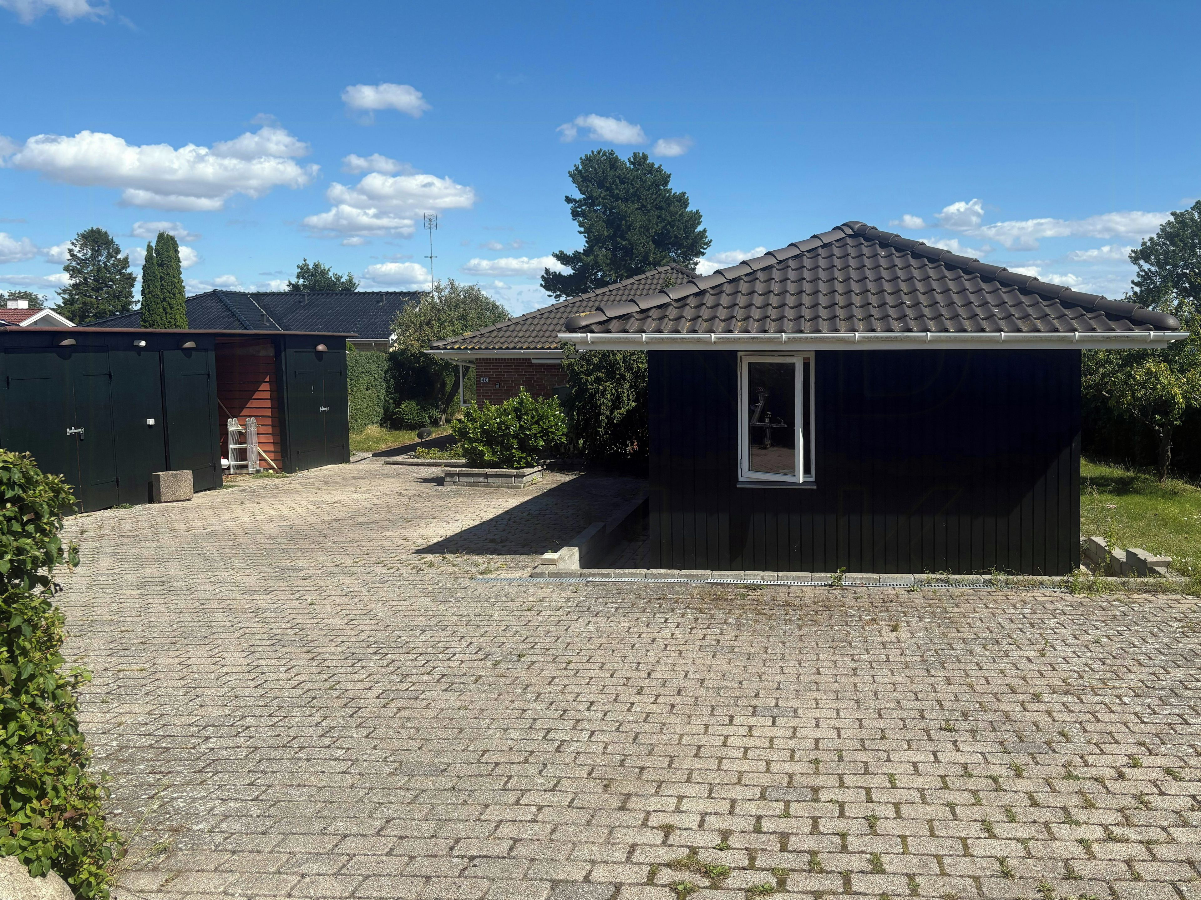 A residential property with a paved driveway, a small shed, and a brick house.