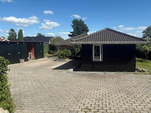 En bostadsfastighet med en asfalterad uppfart, ett litet förråd och ett hus byggt av tegel.