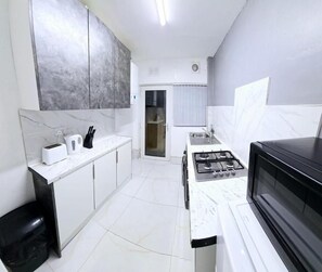A compact kitchen with white cabinetry, a gas stove, a microwave, and a black countertop. - City center 4 bed 8 guest house (Loughborough)