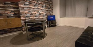 Ett rum med modern design, med en vägg av sten, ett runt bord med metallram, en svart lädersoffa och en tv-skärm som visar Netflix logotyp.