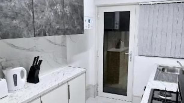 Et moderne køkken med hvide skabe, et marmor bagpanel og en stål bordplade.