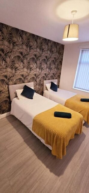 Ett hotellrum med två sängar, en mönstrad tapet och ett fönster med persienner.