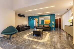 A modern living room with a teal accent wall, two leather sofas, a coffee table, and a unique teal chair. - Matiz Manhattan Hotel - Gym Pool & Sauna (São Paulo)